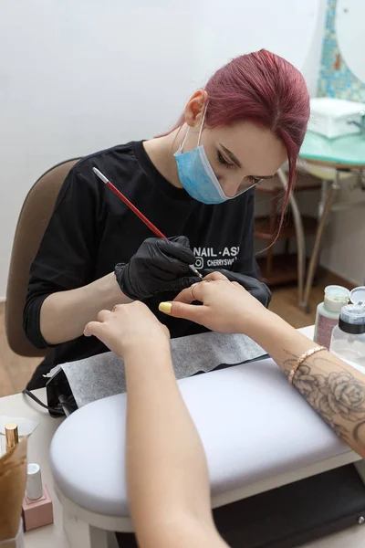 Russland, moskau, 18. mai 2019. nagel master trägt maske und schwarze handschuhe auftragen pinsel auf acrylnägel im salon. — Stockfoto