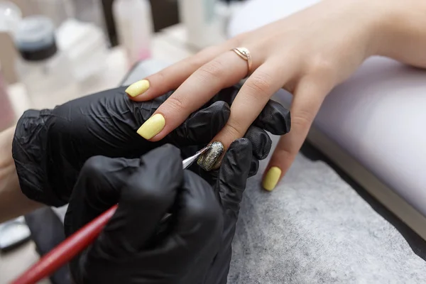 Nail Master bär svarta handskar tillämpa borste på akrylnaglar i salongen. Närbild på manikyr — Stockfoto