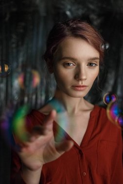 Kırmızı gömlekli sıska genç beyaz kız portresi. Sabun kabarcıkları gökkuşağı renkleri ile parıldayan başının etrafında sinek.