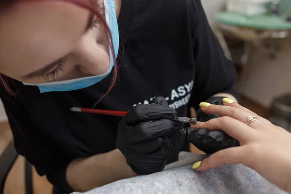 Russland, moskau, 18. mai 2019. nagel master trägt maske und schwarze handschuhe auftragen pinsel auf acrylnägel im salon. — Stockfoto