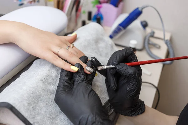 Maître des ongles portant des gants noirs appliquant une brosse sur les ongles en acrylique dans le salon. Gros plan sur la manucure — Photo
