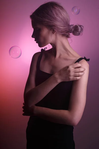 siyah elbiseli şehvetli beyaz kız, pembe arka planda yüzünde gölge. Kafasının etrafında iki sabun köpüğü uçar..