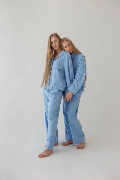 Dos hermanas gemelas muy jóvenes con el pelo largo y rubio posando sobre fondo blanco en ropa de gran tamaño. Sesión de fotos de moda — Foto de Stock