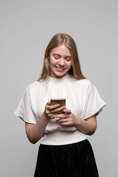 Uzun saçlı genç güzel sarışın kız gülümseyen ve gri arka plan izole cep telefonu kullanarak. Modern iletişim — Stok fotoğraf