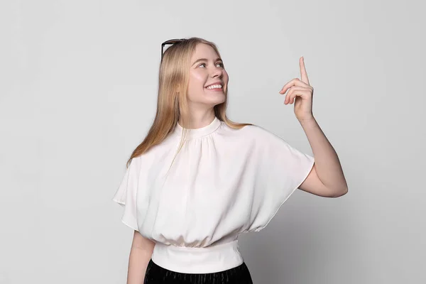 Молодая симпатичная улыбающаяся блондинка в черной юбке на белом фоне показывает пальцем вверх. Место для текста, копирайт — стоковое фото