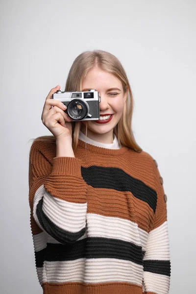 Menina loira bonita nova com lábios vermelhos brilhantes sorrindo, segurando câmera de fotos vintage, tirando foto no fundo branco — Fotografia de Stock