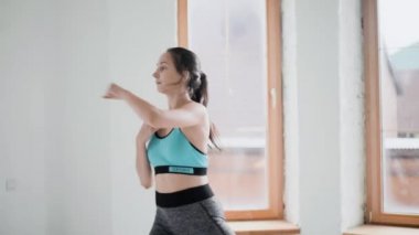 Spor giyimli esmer genç kız parlak odada egzersiz yapıyor. Evde spor yapıyorum. Sağlıklı bir yaşam tarzı. Boks