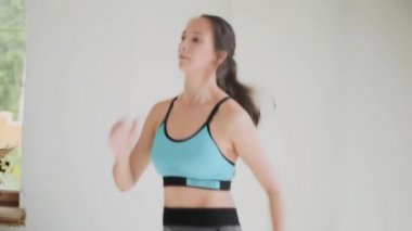 Mavi bluzlu esmer genç kız, tozluklar parlak odada egzersiz yapıyor. Evde spor ve spor eğitimi alıyorum.