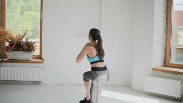 Chica morena en forma joven en ropa deportiva hace ejercicios en habitación luminosa. Hacer deporte en casa. Estilo de vida saludable. Sentadillas — Vídeos de Stock