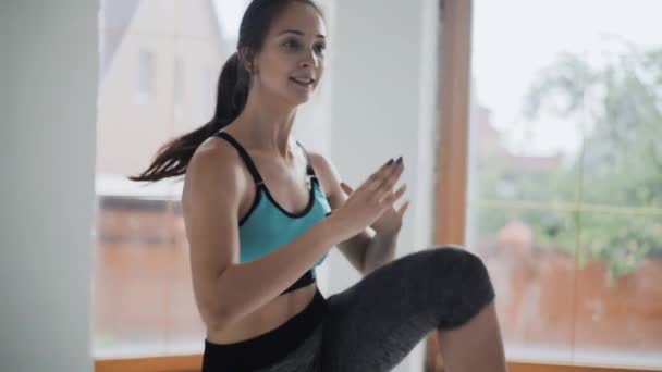 Giovane ragazza bruna in forma in top blu, leggings fa esercizi in camera luminosa. Fare sport e fitness training a casa — Video Stock