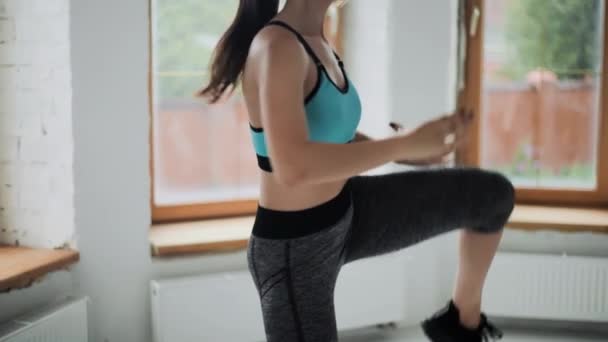 Mladý fit brunetka dívka v modrém top, kamaše dělá cvičení v světlé místnosti. Sportovní a fitness trénink doma — Stock video