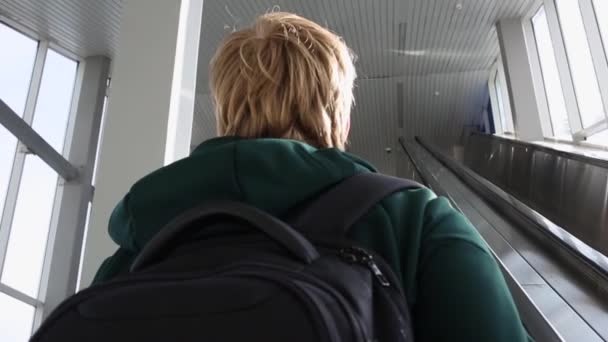 Closeup på unge blonde mænd tilbage ridning op på rulletrappe på solrig dag. Mand med rygsæk stiger op fra metroen – Stock-video