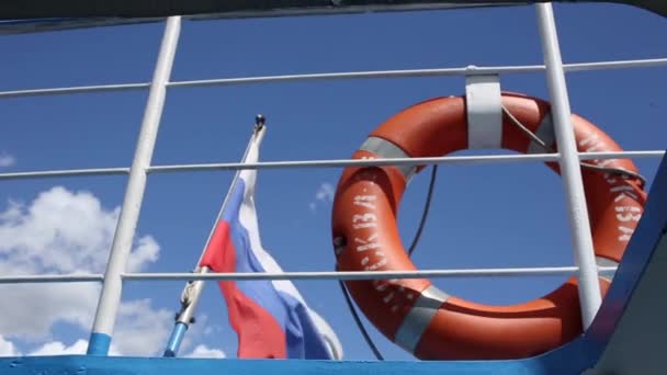 Boia salva-vidas com inscrição Moscou pendurado no corrimão do navio no dia ensolarado. bandeira da Rússia acenando, nuvens no fundo — Vídeo de Stock