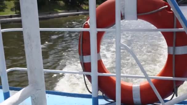 Bouée de sauvetage orange suspendue sur la rambarde du navire par une journée ensoleillée. vagues d'eau en arrière-plan. bateaux à moteur vue arrière — Video