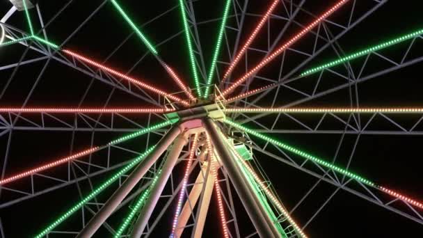 Colorful flickering ferris wheel in amusement park revolves around its axis at night. Visiting attraction at nighttime — Stock Video