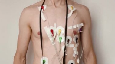 Beyaz arka planda göğsüne bağlı Holter monitörü olan genç, zayıf bir adam. Kablolar yamayla cilde bağlanmış. 24 saat boyunca elektriksel kardiyogram kaydı, sağlık ve kalp sorunları teşhisi