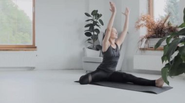 Gri saçlı, atkuyruklu esmer, genç bir kız. Siyah taytlar parlak odada paspas üzerinde egzersiz yapıyor. Evde spor ve spor eğitimi alıyorum. Sağlıklı bir yaşam tarzı. Uzanıyor, öne eğiliyor.