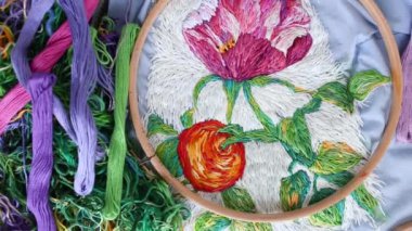 Composition of embroidery hoops, threads and needles on the background of blue embroidered fabric with colorful beautiful pattern. Flat lay, top view. Traditional hobby. Preparing for needlework