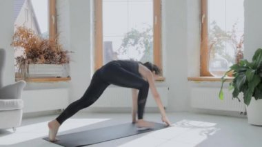 Gri saçlı, atkuyruklu esmer, genç bir kız. Siyah taytlar parlak odada paspas üzerinde egzersiz yapıyor. Evde spor ve spor eğitimi alıyorum. Sağlıklı bir yaşam tarzı. Uzanıyor, öne eğiliyor.