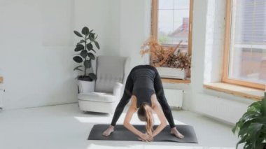 Gri saçlı, atkuyruklu esmer, genç bir kız. Siyah taytlar parlak odada paspas üzerinde egzersiz yapıyor. Evde spor ve spor eğitimi alıyorum. Sağlıklı bir yaşam tarzı. Uzanıyor, öne eğiliyor.