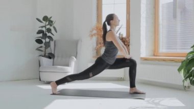 Gri saçlı, atkuyruklu esmer, genç bir kız. Siyah taytlar parlak odada paspas üzerinde egzersiz yapıyor. Evde spor ve spor eğitimi alıyorum. Sağlıklı bir yaşam tarzı. Uzanıyor, öne eğiliyor.