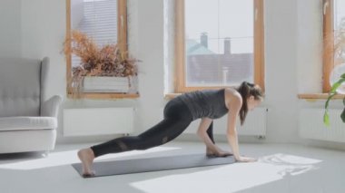 Gri saçlı, atkuyruklu esmer, genç bir kız. Siyah taytlar parlak odada paspas üzerinde egzersiz yapıyor. Evde spor ve spor eğitimi alıyorum. Sağlıklı bir yaşam tarzı. Uzanıyor, öne eğiliyor.