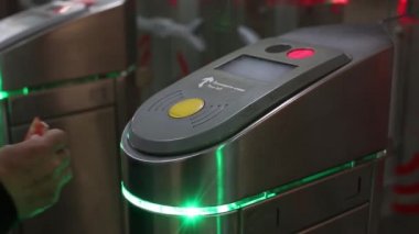 Turnikenin altındaki kırmızı ışık. Biri elektronik kart uygular, yeşil ışık yanar, adam açık kapılardan geçer. Metal kale kontrol paneli, giriş ücretini dokunmatik kartlarla ödeyen insanlar