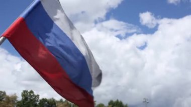 Rus bayrağı rüzgardan dalgalanıyor yeşil ağaçlar ve şehir el fenerleri, güneşli bir günde mavi gökyüzü