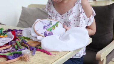 Kafe masasında oturan ve iğneyle dikiş diken yaz elbisesi giyen genç ve güzel bir kız. Nakışlı halka, renkli desenli nakışlı kumaş. Geleneksel hobi, yaşam tarzı. İğne işi, el işi.