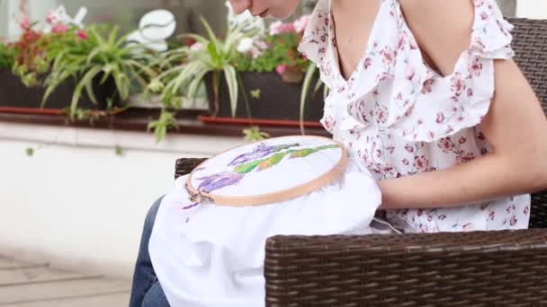 夏のドレスを着た若い可愛い女の子が針でアームチェアの縫製に座っています刺繍フープ カラフルなパターンの刺繍生地 伝統的な趣味 ライフスタイル 針仕事 — ストック動画