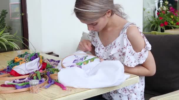 穿着夏装的年轻漂亮的姑娘坐在用针头缝制的咖啡桌旁 绣花花圈 绣花织物与五彩斑斓图案 传统的爱好 生活方式 手工艺品 — 图库视频影像