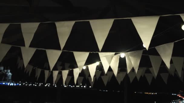 Banderas triangulares blancas en la cuerda colgando al aire libre y balanceándose en el viento por la noche — Vídeos de Stock