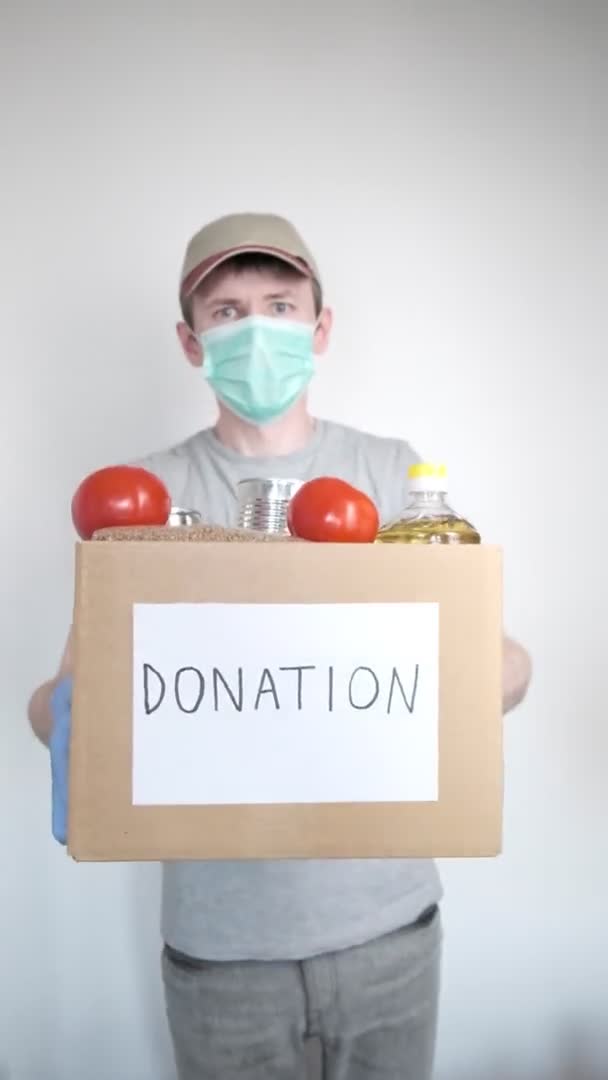 İlaç koruyucu maske gönüllüsü karton bağış kutusunda market yemekleri gösteriyor. — Stok video