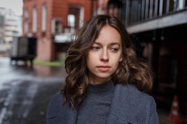 Gri montlu ve balıkçı yakalı güzel kız kırmızı binanın önünde poz veriyor. Çekici bir kadının sokak fotoğrafı, zarif bir modelin şehir fotoğrafı.