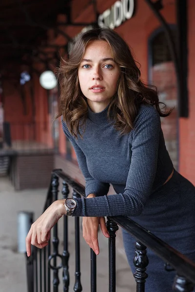 グレーのタートルネックの若い思慮深い可愛い女の子赤い建物の前の腕時計のスカート 魅力的な女性のストリートスタイルの肖像写真 エレガントなモデルの都市の写真 — ストック写真