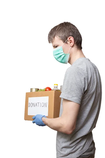 Волонтер в синіх захисних рукавичках тримає продовольчу їжу в коробці для пожертвувань — стокове фото
