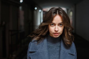 Gri montlu ve balıkçı yakalı genç ve düşünceli kızın açık havada poz vermesine yakın çekim. Çekici bir kadının sokak fotoğrafı, zarif bir modelin şehir fotoğrafı, yakın çekim.