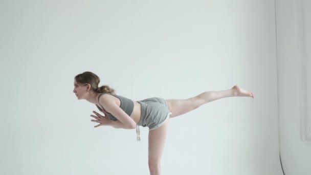 Jong meisje in sportkleding balanceert op een been in yoga asana. pilates, uitrekken — Stockvideo