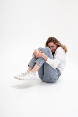 Beyaz gömlekli gülümseyen beyaz bir kız, stüdyoda kot pantolon giyiyor.