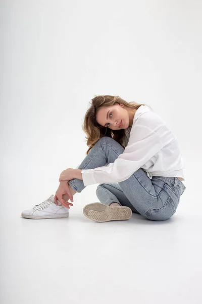 Beyaz gömlekli, mavi kotlu beyaz bir kız stüdyoda poz veriyor.