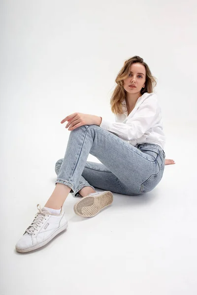 Giovane ragazza caucasica pensosa carina in posa in camicia bianca, jeans blu in studio — Foto Stock