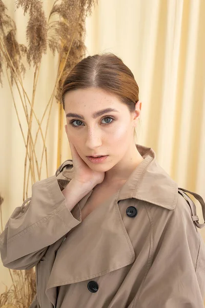Pretty woman in beige raincoat on pastel fabric background. fashion photo shoot — Stock Photo, Image