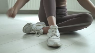 Spor giysili genç bir kız dizlerinin üzerinde oturuyor, ayakkabı bağcıklarını spor ayakkabılarına bağlıyor.