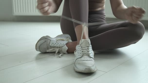 膝の上の床に座ってスニーカーに靴ひもを結ぶスポーツウェアの少女 — ストック動画