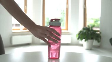 Kadın parlak odadaki masaya pembe plastik su şişesi koyuyor, yakın plan.