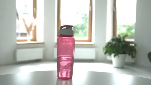 Kvinna tar rosa plastflaska vatten från bordet i ljust rum, närbild — Stockvideo