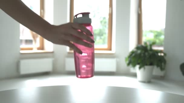 Vrouw zetten roze plastic fles water op tafel in lichte kamer, closeup — Stockvideo