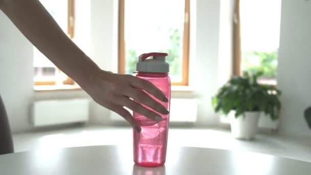 Kvinna sätta rosa plastflaska vatten på bordet i ljust rum, närbild — Stockvideo