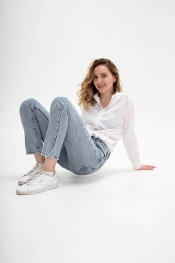 Beyaz gömlekli, mavi kotlu beyaz bir kız stüdyoda poz veriyor.