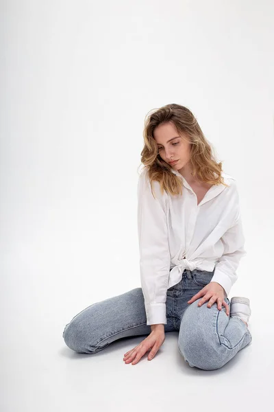 Joven lindo pensamiento chica caucásica posando en camisa blanca, pantalones vaqueros azules en el estudio — Foto de Stock